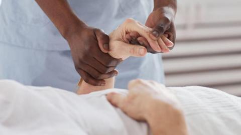 A black hospital worker holds the hand of an elderly white patient.