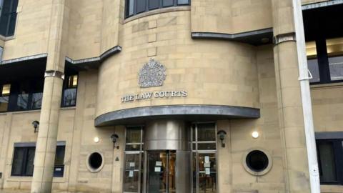 The exterior of the Bradford Crown Court building, with light coloured stone and silver letters of "The Law Courts" written on the front. 