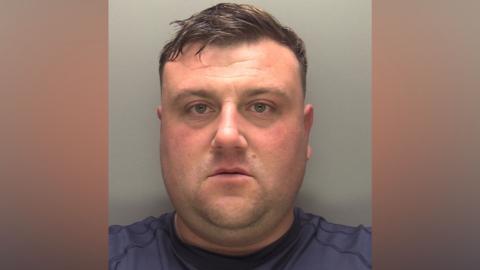 Police custody photograph of Lathan Middleton. He has short dark hair and is wearing a blue top.