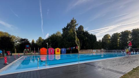 An outdoor swimming pool with bright blue water and colourful beachhuts at the side