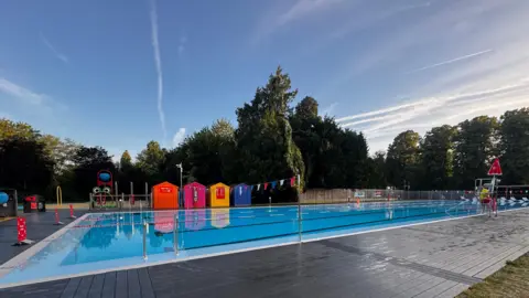An outdoor swimming pool with bright blue water and colourful beachhuts at the side