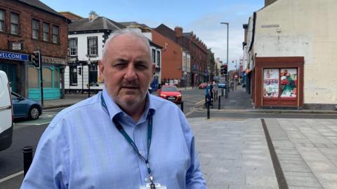 Mark Fryer, who has short grey hair and is wearing a blue shirt, looking at camera from bottom of Carlisle's Botchergate street.