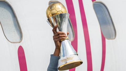 The 2024 Women's Africa Cup of Nations trophy - a sleek silver trophy with gold trim and topped with a golden football - is seen being held aloft by a single hand