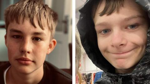 Max Dixon and Mason Rist. Mason is wearing a black crew neck jumper and has dark eyes and brown hair in a downward fringe. Max is wearing a black raincoat with his hood up and is smiling downwards, with pieces of his fringe peeking out. 