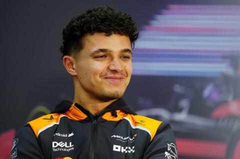 Lando Norris, wearing his McLaren kit, is sitting and smiling during a break in pre-season testing in Bahrain