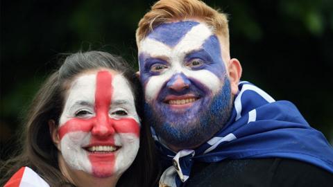 A woman with an England flag painted on her face poses with a man with a Scotland flag painted on his face