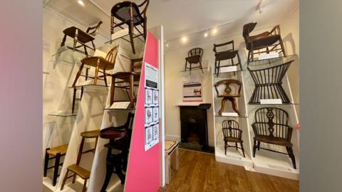 Wooden chairs on display at different heights in a museum room