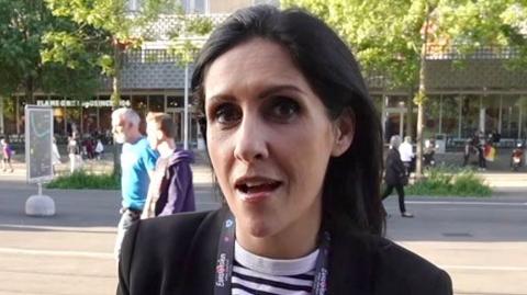 BBC News presenter Maryam Moshiri speaks to the camera while standing outside, with a UK flag graphic embedded onto the image.