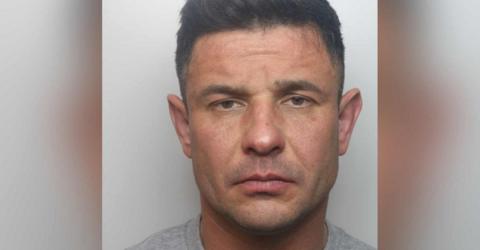 Police mugshot of Jakub Nowicki looking at the camera. He has dark hair and wears a police issue grey t-shirt.