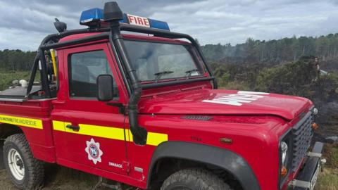 A red 4x4 fire vehicle parked in an area of charred heathland and gorse