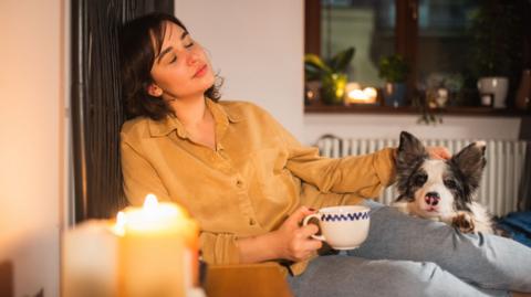 
Young woman relaxing at home with her dog in bed with candles and hot drink