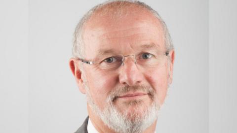 Headshot of Stephen Davies wearing a grey suit with a white shirt and multi-coloured tie