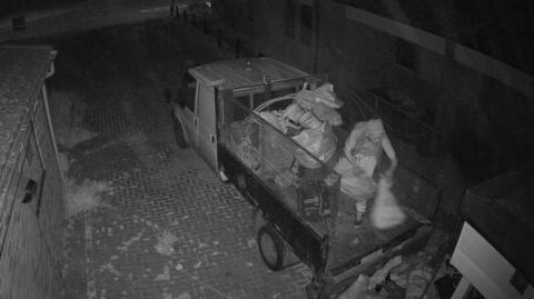 Footage shows a man wearing a hoodie and standing in the back of his van throwing bags of rubbish onto the floor.