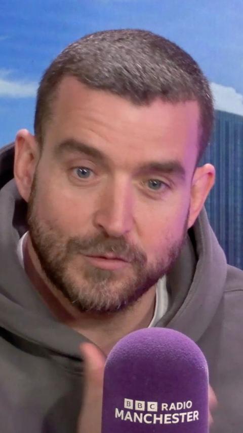 A man with short brown hair is sat behind a microphone which says BBC Radio Manchester