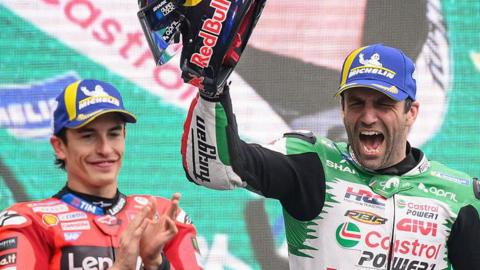Marc Marquez applauds as Johann Zarco celebrates on the podium after winning MotoGP's 2025 French Grand Prix