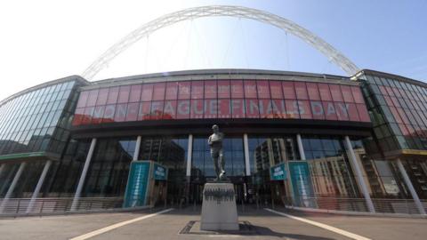 The front of Wembley Stadium. There is the statue of Bobby Moore in front of the main entrance with the arch in the top of the picture and a sign behind the statue which says "non-league finals day".