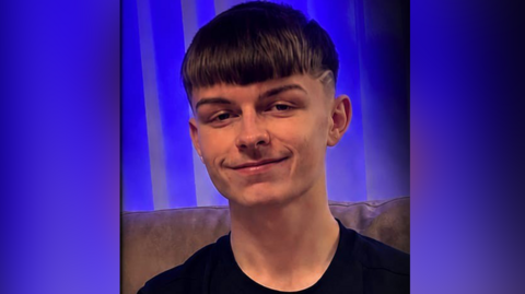 A teenage boy smiling at the camera. He has short brown hair and a black t-shirt on. 
