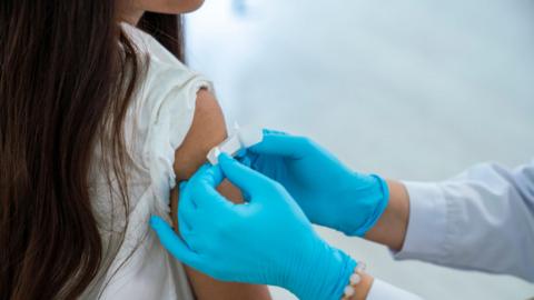 A young girl is has a plaster put on her arm by a person wearing blue gloves