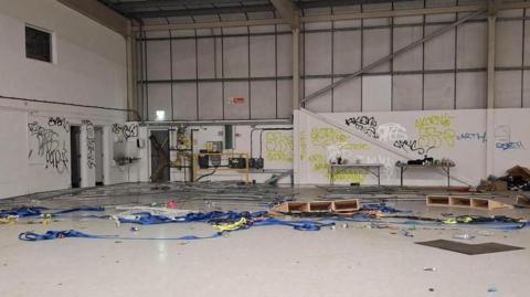 An empty industrial unit has graffiti on the walls and what looks like blue banners on the floor