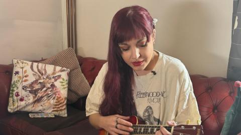 A young woman with red hair playing a ukulele