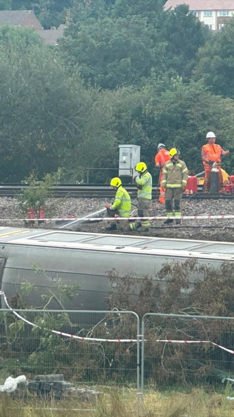 Fighfighters spraying water from hose on derailed train