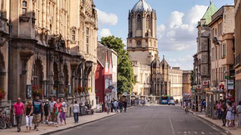 A busy street in Oxford. Christ Church cathedral can be seen rising above the rooftops.