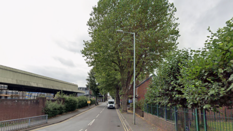 A road is near the bottom of this generic image on the left. A large tree is prominent in the middle of the photo and part of a house is visible to the right of it.