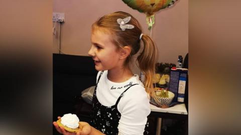 Lilia Valutyte. She is wearing a white top and has a cake in her hand.
