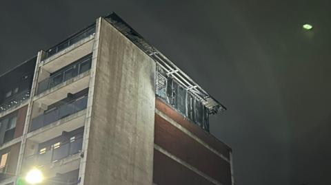 The side of the fire damaged building at the top of the building taken on Thursday morning - with a dark sky in the background 