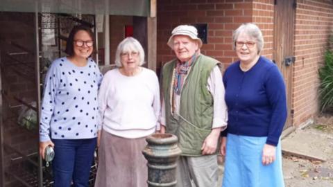 Three women and a man stand in a line together outside a post office