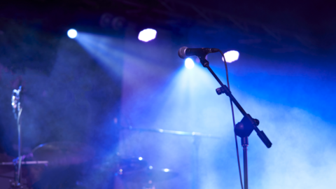 A microphone can be seen on a stage with lighting above and below and smoke ready for a performer or band to come on stage.