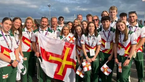 A group shot of people smiling and holding Guernsey flags. 