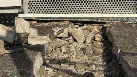The damaged pavement, with a trench filled with smashed up concrete blocks.