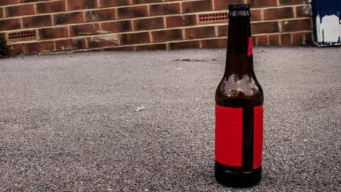 Stock image of a beer bottle on a street, with a brick wall in the background.