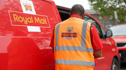 A red Royal Mail van and a man in an orange vest stood next to the parked vehicle.