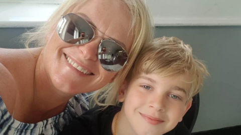 A woman smiles while sitting with a young boy. He has blonde hair like his mother. They look happy together.