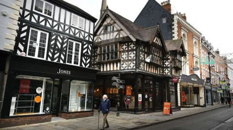 An old black and white timber building features on a street in the town among other high streets shops