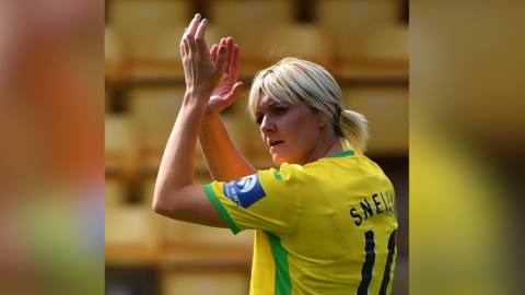 Striker Natasha Snelling in a Norwich City shirt which has the number 10 and SNELLING on the back. She is looking towards the left and is clapping into the air above her head.