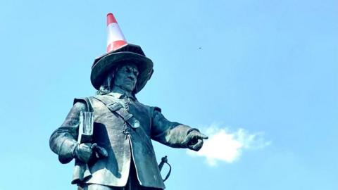 A red and white traffic cone on top of a staue of Oliver Cromwell