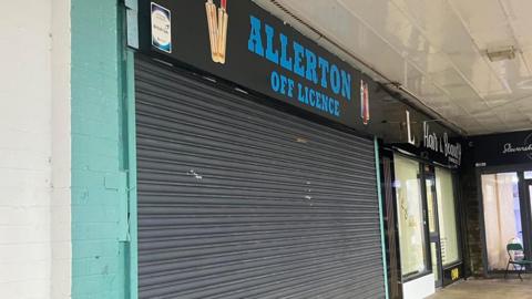 A shop with its black shutters pulled down, indicating it is closed.