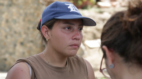Andreina Valerio, in a blue baseball cap, stands in front of rubble