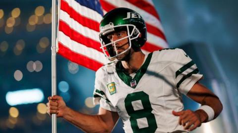 Aaron Rodgers runs onto the field for his New York Jets debut carrying an American flag
