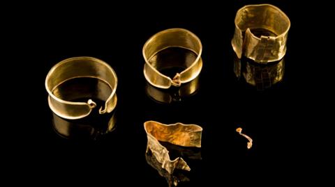 Gold jewellery dating back to the Bronze Age laid out on a black surface.