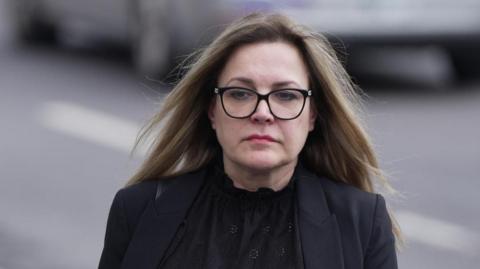 A woman wearing glasses and a black suit.