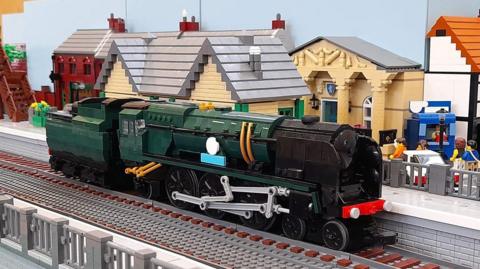 Green locomotive made out of Lego on brick tracks