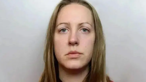 A custody photograph of Lucy Letby who has long blonde hair and and is wearing a red top.