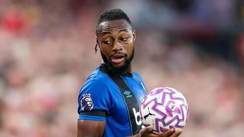 Antoine Semenyo holds a ball as he plans to make a throw-in. He looks over his right shoulder and is wearing the blue and black striped Bournemouth shirt.