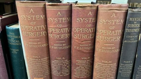 A row of old medical books, including four volumes of A System of Operative Surgery.