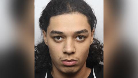 Police custody image of Harvey Bell with long dark hair and brown eyes wearing a black top.