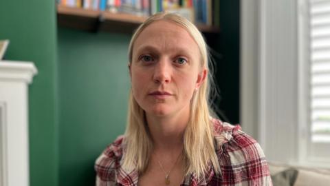 A woman with blonde hair and a red checkered shirt. She looks melancholic. 